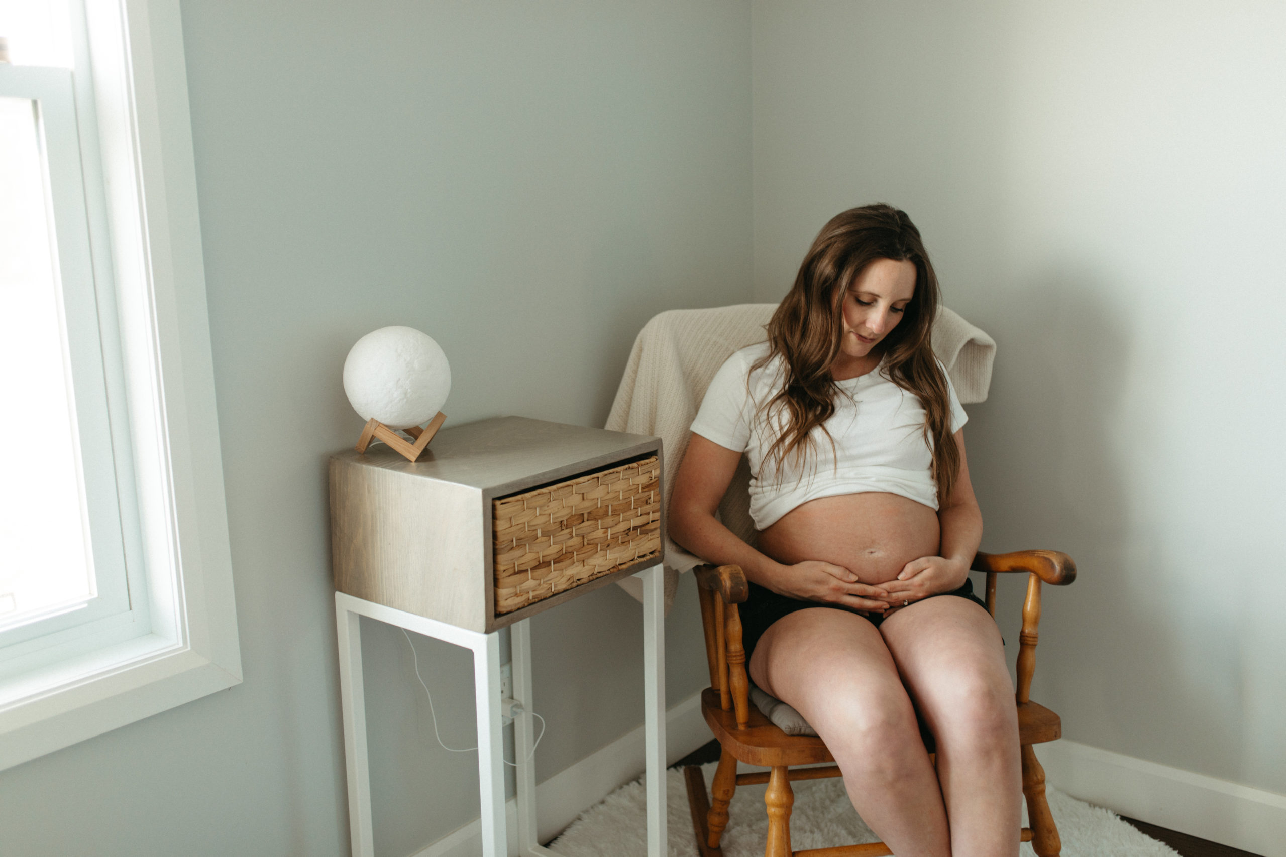 Maternity Photo at home pregnant women sitting on a chair place her hands on her pregnant belly