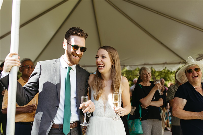 Couple in wedding attire smiling at each under a tent